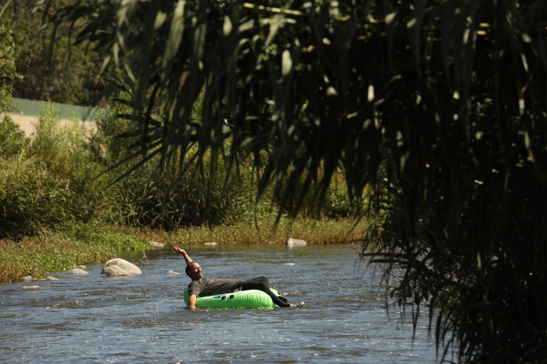 A man floats on a lime-green raft on the L.A. River 